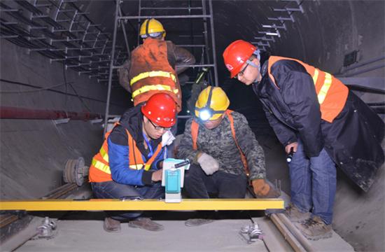 隨著我國公路建設規模的日益擴大，公路隧道建設取得了很大的發展,公路隧道具有斷面大，地質條件和施工技術復雜等特點，加之設計時對地質條件的認識不夠全面準確，通車后存在的隧道老化、運營管理和維護等方面的原因，致使我國公路隧道的病害問題十分嚴重，隧道襯砌背后的空洞問題就是其一，由此引起的拱頂上鼓及襯砌內緣壓裂、掉塊的現象嚴重影響到公路隧道的使用壽命。因此加強對隧道襯砌背后空洞的檢測判斷和處理，是隧道工程病害處理的重要一環。 一、檢查目的和必要性 目的：隧道拱部襯砌出現空洞剝落掉塊直接危及行車安全，但襯砌內部病害隱蔽，無法通過肉眼發現，通過人工敲擊可有效發現襯砌內部空洞等隱患，并對無損檢測資料有針對性的進行驗證。 必要性：通過隧道找部襯砌人工敲擊檢查?？蓪Υ蟛糠止安坎『霸绨l現并進行整治，從而降低運營期間拱部襯砌剝落掉塊的風險。 二、檢查時機和范圍 1、檢查時機 隧道二次襯砌貫通后，接觸網安裝前為最佳檢查時機，接觸網安裝后通電前次之，通電后則須停電 。 2、接觸網安裝前、后敲擊檢查的區別 接觸網安裝前后，敲擊方法、車輛、工具基本相同。主要區別： （1）接觸網作業車檢查平臺，升起高度或檢查架搭設高度不同，接觸網安裝前接觸網作業車檢查平臺升起高度或檢查架搭設高度距拱頂3米左右，拱頂至拱腰均易于敲擊，接觸網安裝后接觸網作業車檢查平臺升起高度，或檢查架搭設高度距離拱頂至少4米。 （2）檢查槌長度不同。接觸網安裝前檢查槌長度為2米左右，接觸網安裝后檢查槌長度為2.5米至4.6米。 3、檢查范圍 當使用供電檢查車或軌道車平板上搭檢查架檢查時，從拱頂中心線至起拱線半幅為一次敲擊檢查范圍，當使用檢查架檢查時，從線路左側起拱線至線路右側起拱線全幅為一次敲擊檢查范圍。 圖片描述(最多50字) 三、檢查前準備工作 1、車輛：接觸網檢查車，平板車搭檢查架，在鋼軌或側溝蓋板上推進檢查架，以雙線隧道，軌頂至拱頂9米為例，且檢查平臺距接觸網立柱等侵限物體保持10至20厘米間距。 （1）采用接觸網檢查車檢查無接觸網時，檢查平臺高度以距拱頂3米為宜，檢查平臺橫向放置，有接觸網時，檢查平臺高度以距拱頂5米為宜，檢查平臺縱向放置，需要時再旋轉到橫向位置。 （2）平板車搭檢查架，鋼軌上安裝檢查架或側向水溝蓋板和兩線間底板頂搭設檢查架，無接觸網時，檢查平臺高度以距拱頂距離3米為宜，檢查平臺橫向寬度可達9米，有接觸網時，檢查平臺高度距離拱頂4米為宜，兩線間平臺需下凹0.5米，檢查平臺橫向寬度可達9.5米。 圖片描述(最多50字) 2、工具：大型工具有：接觸網檢查車、軌道車（含平板車）、檢查架（根據凈空定制）；小型工具有：手提式強光手電筒、頭部礦燈、檢查槌（空心鋼管直徑30mm，一端焊接一根尖頭鋼筋一端焊接一根平頭鋼筋，長度2至4.6米不等），卷尺、塞尺、鋼直尺、噴漆、桶裝油漆、漆桿（4.5米長竹竿一端綁扎油漆刷）、檢查梯、對講機、照相機、手套、安全帶、安全帽、防護衣、護目鏡、口罩、記錄本、黑水筆等。 3、人員：作業小組由8人組成（使用接觸網檢查車或軌道車時需1人持對講機指揮車輛），檢查車分工為：3人持檢查槌（敲擊半幅拱頂線路正上方拱腰，線路側方拱腰至起拱線），2人聽敲擊音并標記，1人記錄并拍照，1人指揮并負責安全檢查和提示，檢查架分工為：4人持檢查槌敲擊拱頂、拱腰，2人聽敲擊音標記并負責指揮及安全檢查提示，2人記錄并拍照。 四、敲擊檢查程序 1、開窗安排：提前一天申請檢查天窗，天窗時間本線封鎖不少于8小時，鄰線限速每小時20公里，根據批準的天窗計劃，駐站聯絡員在《行車設備登記簿》內登記，列車高度員下達調度命令；施工負責人接到調度命令后按調度命令憑證發車；檢查車到指定地點后，立即設置防護體系。在距離檢查地點20米處現場防護員設置移動停車信號彈（燈），在距離施工地點800米兩端防護員設置顯示停車手信號；鄰線防護需設置移動減速信號牌和減速地點標。天窗作業計劃結束前機車返回申請?？奎c。駐站聯絡員與現場防護員在執行防護任務時，應佩戴標志攜帶通信設備，現場防護員還應攜帶必要的防護用品；隨時掌握現場和列車運行情況。發現異常情況及時通知車站值班員和施工負責人。駐站聯絡員應與現場防護員時刻保持聯系。 圖片描述(最多50字) 2、敲擊作業：車輛行駛速度控制在每小時5公里以內，檢查架推進速度控制在每小時1公里以內，行進過程中進行敲擊，憑敲擊聲音辨別是否存在空洞，聲音異常時停車仔細敲擊確認空洞范圍，施工縫、混凝土修補、蜂窩、混凝土表面有雜物（如鋼筋頭、注漿管等）、施工冷縫、止水帶外露、防水板外露、閉環裂紋、變形外鼓等重點處所均停車進行仔細敲擊檢查。 3、照明配置、照度、范圍：BAD305手提式防爆探照燈2臺，BAD212微型手持防爆調光工作燈2臺，LED722B充電頭燈2臺，照度不低于250勒克斯，照明可視距度10m。 4、敲擊人員自我防護注意事項：（1）作業前將勞動防護用品穿戴整齊‘（2）攀爬腳手架時，要站穩扶牢。登上檢查平臺后，須首先掛好安全帶和安裝欄桿扶手，工具應放置穩固。（3）接觸網檢查車檢查平臺、檢查架移動前應通知作業人員停止作業，將工具擺放穩固，人員蹲下扶牢，目視前進方向，機車指揮人員發現侵限物體要及時停車，拆除侵限物體。檢查架移動就位后，必須設好滾輪制動和斜撐后，方可作業。（4）檢查小組人員必須團結協作、聽從指揮，相互提醒安全注意事項，做到自控、互控。（5）人員站位要相對固定，避免檢查槌等工具碰傷人員。（6）清除襯砌掉塊時，應高聲提醒所有人員注意安全，下方無人時，方可進行作業。（7）鄰線來車時，須停止作業，小穩扶牢，檢查工具不得侵限。 5、檢查架的組成：同槽鋼跑道、腳手架滾輪及抽動裝置、 鋼管立柱、鋼管橫撐、鋼管斜撐、十字卡、萬向卡、腳手板及鐵絲、欄桿及鎖口鋼筋、反光標等組成。 6、缺陷確認：敲擊聲音清脆，發出“鐺、鐺、鐺”的聲音說明襯砌混凝土比較密實，如果敲擊聲音沉悶出現“咚、咚、咚”的聲音，說明襯砌混凝土存在空洞，附帶檢查內容包括襯砌掉塊、裂紋、滲漏水、露筋、鋼筋保護層厚度不足、蜂窩麻面、混凝土夾帶雜物等。 7、問題標記：發現問題停車采用紅油漆標記問題范圍，測量（估算）相關尺寸，將病害類型、尺寸等數據詳細記錄、拍照存檔，如在空洞外邊界標記面積范圍，在裂縫起終點位置用箭頭（箭頭朝向裂紋處）標記長度，箭頭旁標出裂紋寬度值，同時將問題類型、編號、里程用紅油漆在問題位置邊墻上進行標記，以便日后整改。標記形式“BLWKD-1-K493+179”，BLW指白力塢隧道，KD指拱部空洞，1指編號為1號，K493+179指空洞里程，若一個隧道有多處空洞，序號按里程從小到大排序，依次為1、2、3、4.......。 8、資料整理：為避免出現場檢查發現問題記憶模糊、相似問題相互混淆的情況，檢查小組每天須將當天檢查發現的問題，根據病害類型、部位、按靜態驗收報告格式進行梳理、統計，將照片編輯相應文字說明。